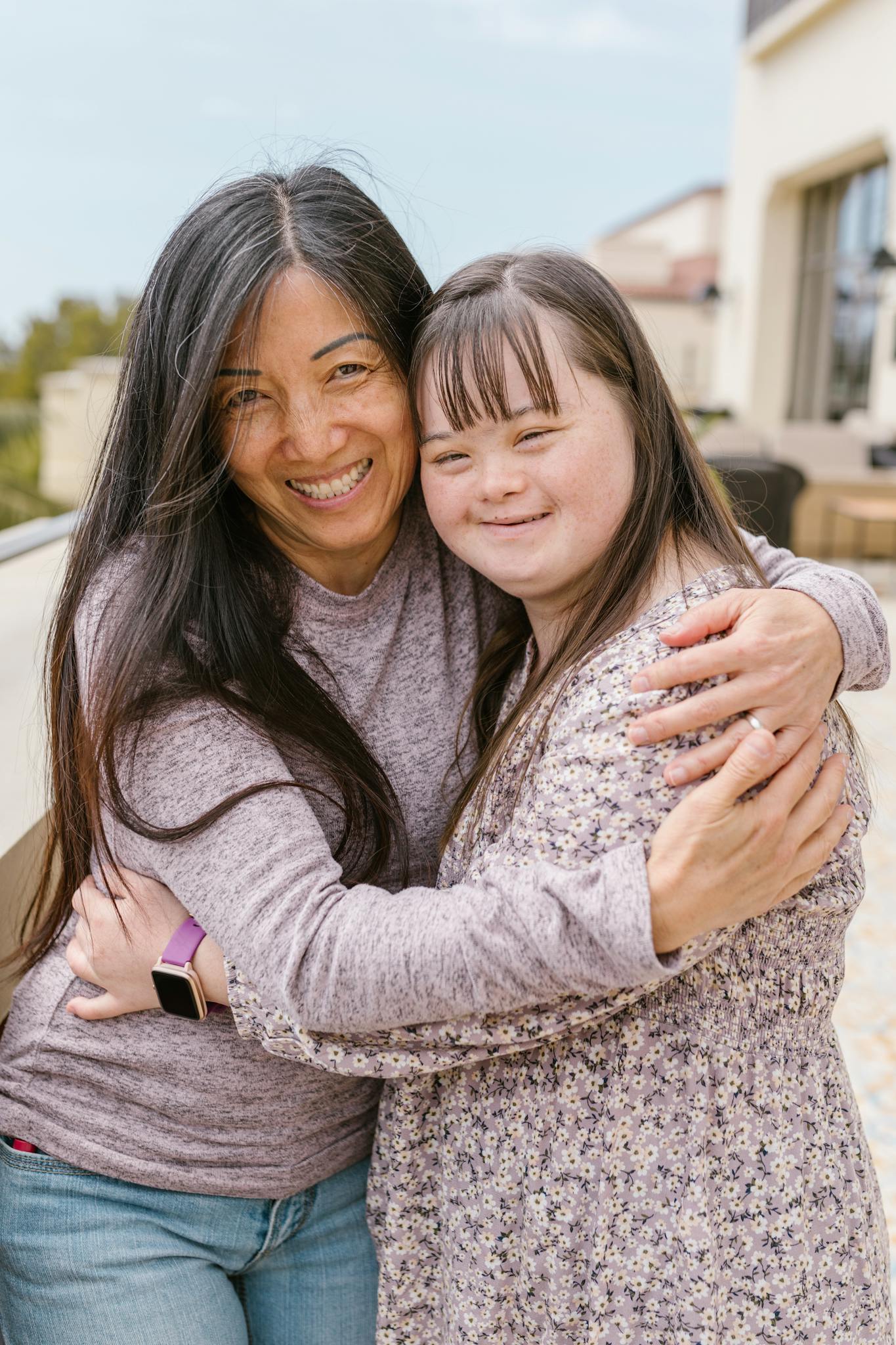 A joyful moment of a mother and daughter with Down syndrome sharing a warm embrace outdoors.