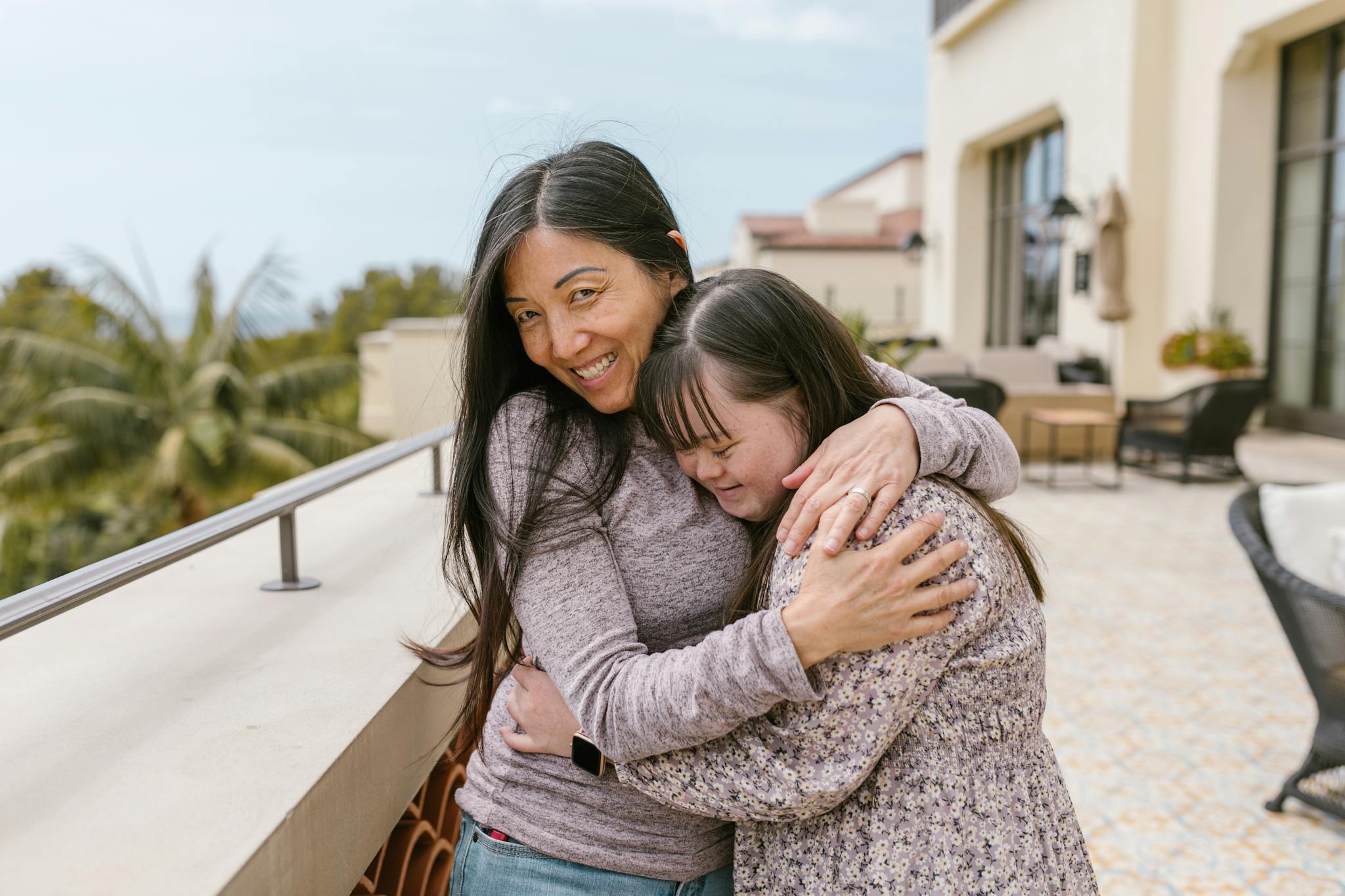 Mother and daughter with Down syndrome share a warm embrace outdoors on a sunny day.