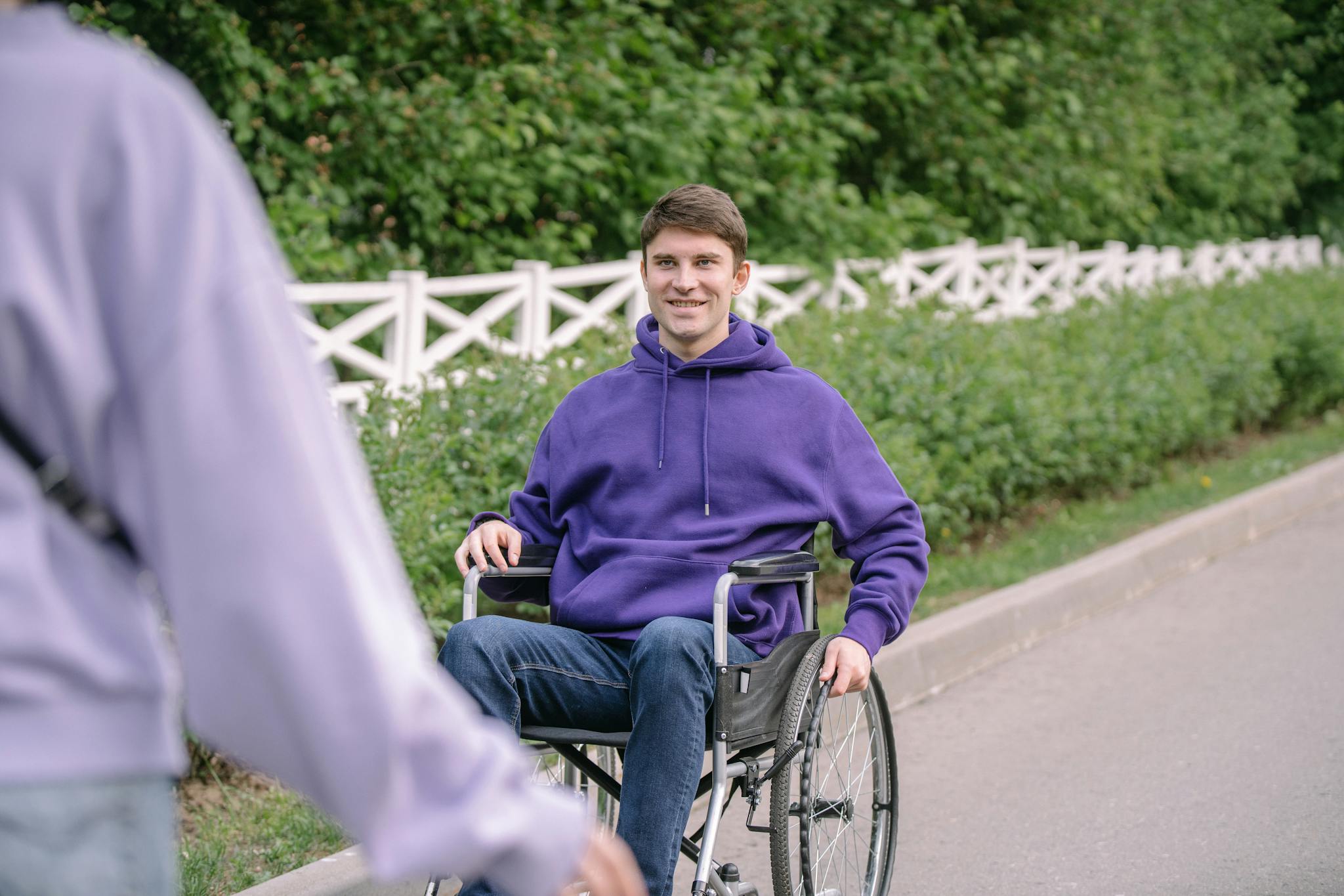 Portrait of a man in a wheelchair wearing a purple hoodie, smiling outdoors.